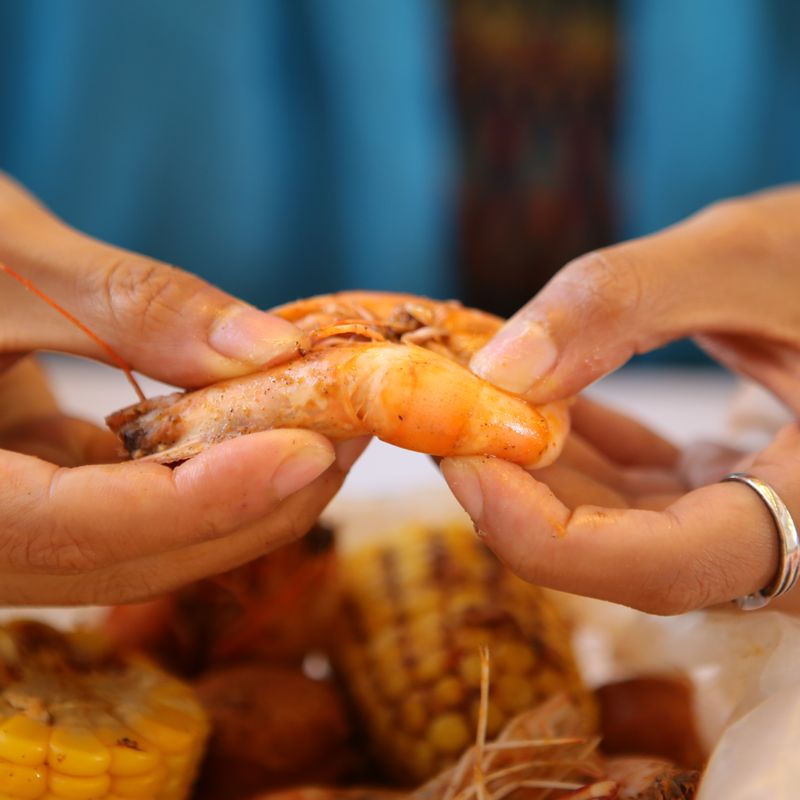 Two hands peeling a boiled shrimp over corn