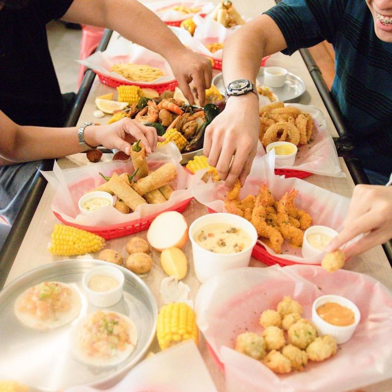 Friends reaching across a long table of seafood, fries, corn and dips