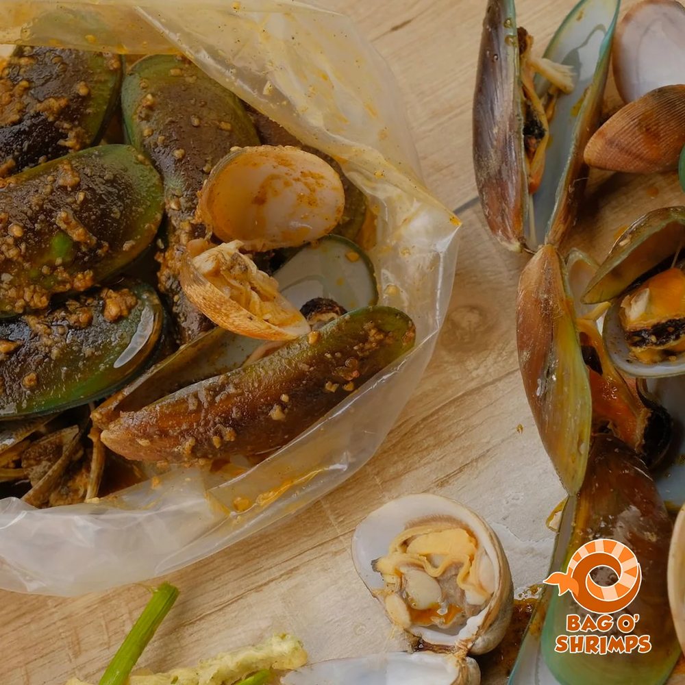 Mussels and clams in a spiced garlic sauce, spilling from the bag
